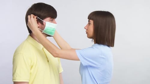 Woman Puts Surgical Mask on Man in Studio