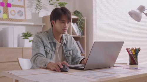 At home, a business asian man types and works online on a desk table with a laptop.