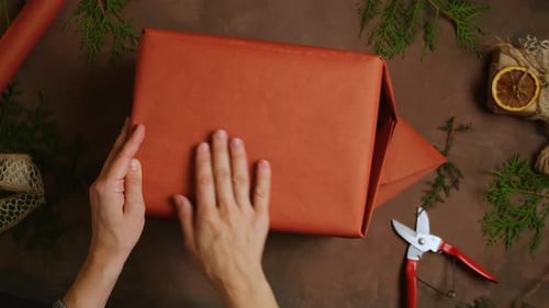 Hands Wrapping Christmas Gift with Terracotta Paper