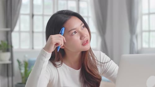 Woman Works at Laptop, Holds Pen to Head