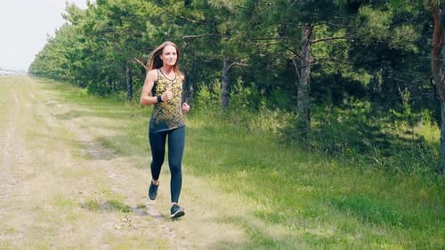 Young Pretty Girl Goes in for Sports in the Morning, Runs Along a Pine Forest. She Smiles.