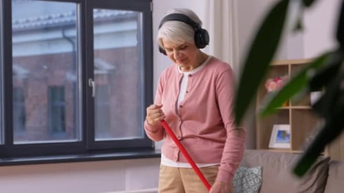Old Woman in Headphones with Broom Sweeping Floor