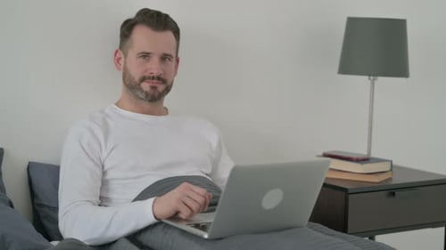 Homme avec un ordinateur portable montrant les pouces vers le haut au lit