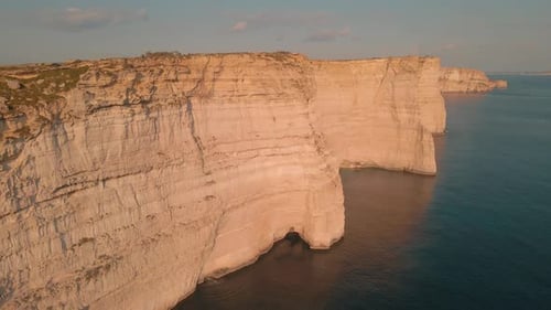 Stunning limestone cliffs of Malta reflect off the water of the Mediterranean Sea as the drone shot