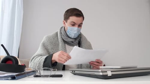 Man with Mask Reads Papers at Desk