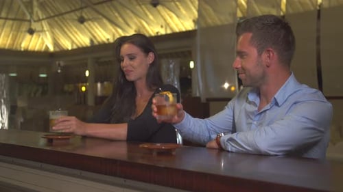 A man and woman couple toasting a cold drink at a bar at a tropical island resort