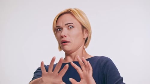 Femme blonde caucasienne d'âge moyen effrayée en sweat-shirt bleu jouant à la pantomime en poussant sur blanc