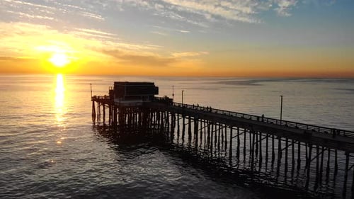 Drone footage over Newport beach pier with people in silhouette during a scenic southern California