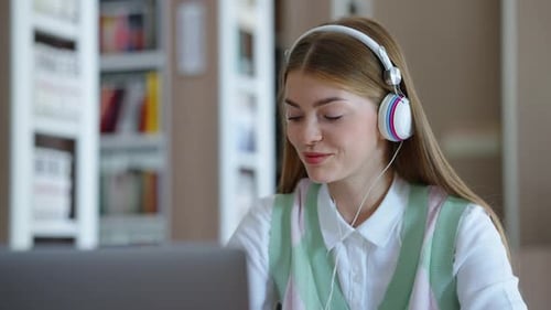 Student Works on Laptop in Library With Headphones