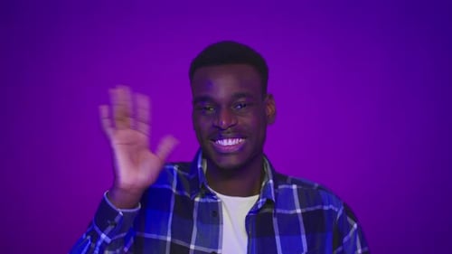 Happy African Guy Waving Hand Gesturing Hello Over Purple Background