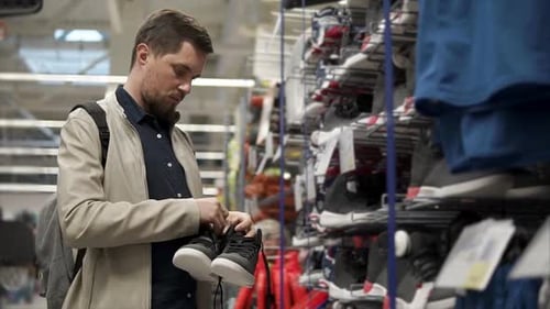 Male Shopper is Watching Pair of Sneakers in a Sales Area in Sport Store