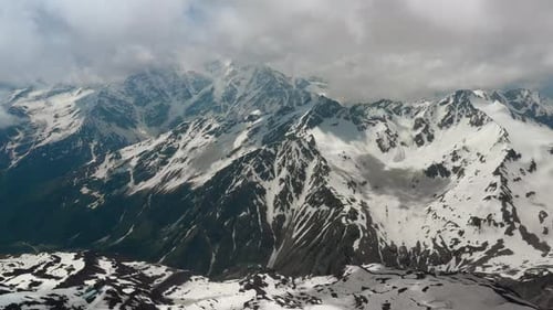 Air Flight Through Mountain Clouds Over Beautiful Snowcapped Peaks of Mountains and Glaciers