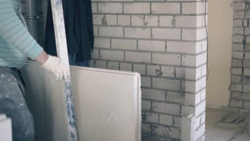 Man Holds Plasterboard Against Brick Wall Indoors