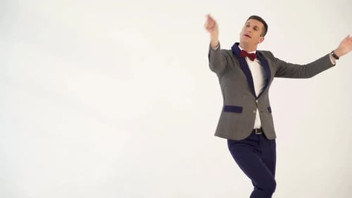 Humorista de traje gris con pajarita roja baila a semejanza de una bailarina