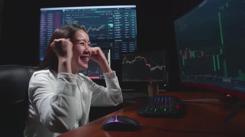 Asian Female Stock Market Broker Working On Computer And Celebrating With Analysing Graphs