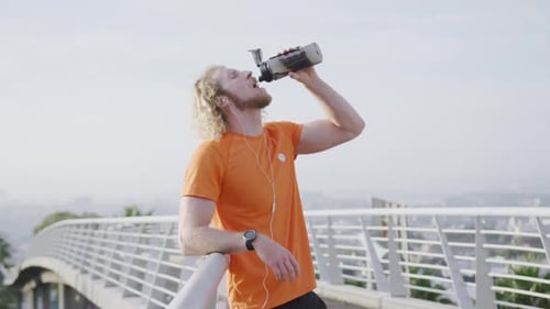 Athletic Man Drinking Water on Pedestrian Bridge