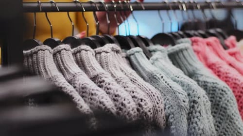 Closeup Clothes Hanger with Colored Sweaters in Clothing Store Female Hands Sorting Clothing