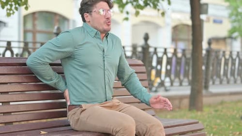 Man on Bench Experiences Back Pain Outdoors