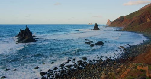 Large Waves with Foam Roll on Hilly Ocean Rocky Beach at Sunset