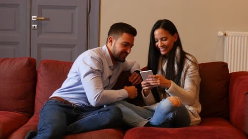 Couple Relaxing on Couch, Using Smartphone Together