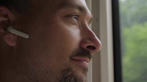 Man Looking out Window with Wireless Earbud