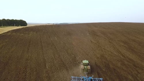 Aerial footage of a tractor plowing black agriculture farm field after harvesting in autumn.