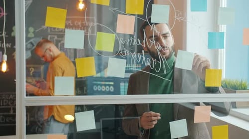 Porträt eines jungen Geschäftsmannes, der mit Glasbrettern arbeitet und auf Haftnotizen schreibt
