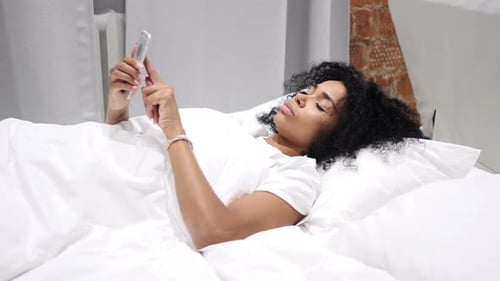 Woman Using Cell Phone in Bed Under Sheets