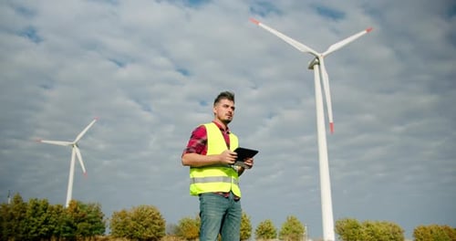 Der Ingenieur arbeitet mit dem Tablet in der Hand neben den Windmühlenturbinen