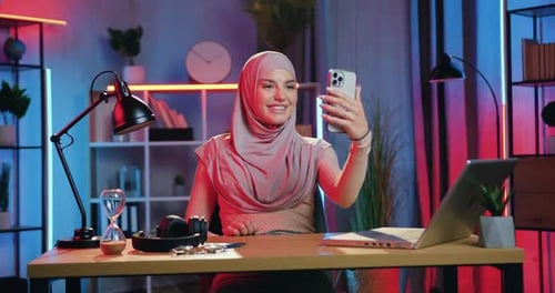 Mujer en hiyab disfrutando de una agradable charla de Vídeo con un amigo o familia en una habitación bellamente iluminada