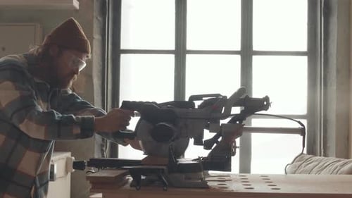 Man Cuts Wood With Miter Saw in Workshop