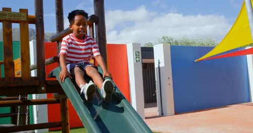 Front view of African American schoolboy playing on slides in the school playground 4k