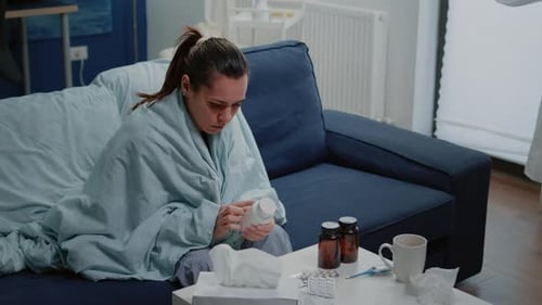 Woman Examining Medication Bottle at Home Feeling Ill