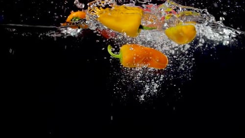 Colorful sweet peppers being dropped into water in slow motion.