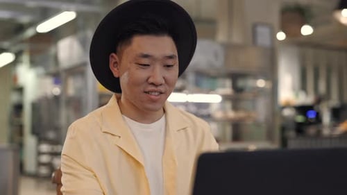 Glücklicher junger Mann, der im Café sitzt und am Laptop arbeitet