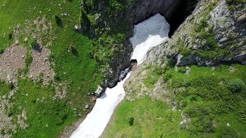 Blick von oben auf steile Bergklippen und eine Eishöhle