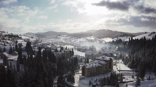 Luftaufnahmen eines kleinen Bergdorfes im Winter bei sonnigem Tag mit epischen Wolken