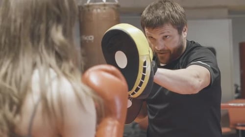 Woman Punching Pads with Trainer in Indoor Gym