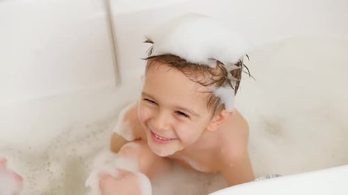 Nahaufnahme einer jungen Mutter, die mit ihrem kleinen Sohn spielt, ein Bad nimmt und Haare mit Shampoo wäscht