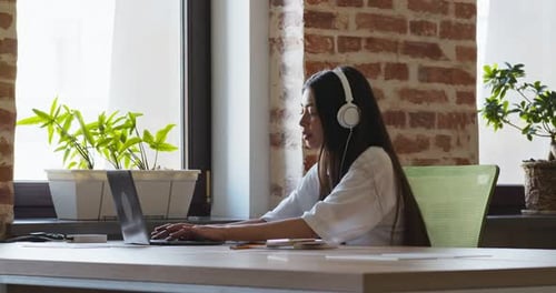 Woman Typing on Laptop with Headphones at Desk