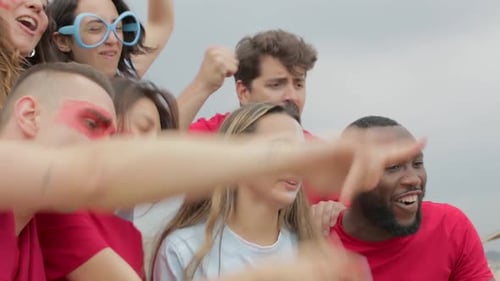 Multiracial group of spectators in team colours watching sports event at stadium