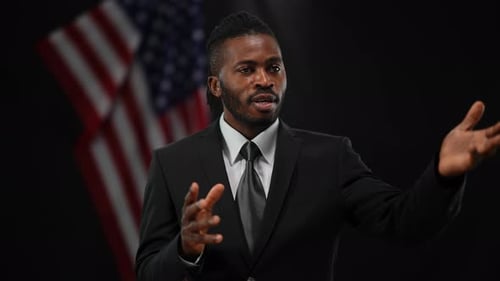 Persuasive Confident African American Man Talking and Gesturing with Blurred US Flag at Black