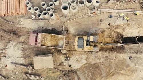 Aerial view of excavator pours sand into the truck. On the construction site top view. Shooting from