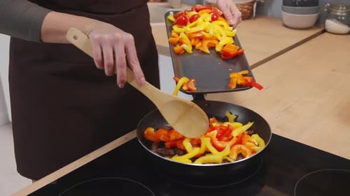 Adding Sliced Peppers to Frying Pan in Kitchen