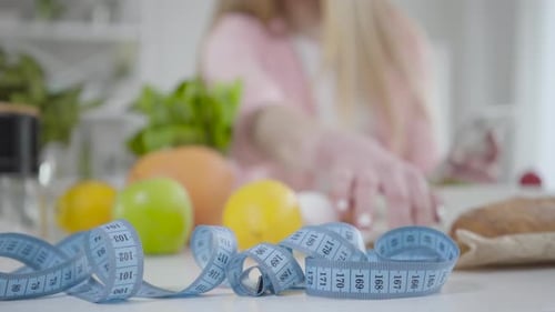 Close-up of Measuring Tape Lying on the Table with Blurred Caucasian Girl Counting Calories