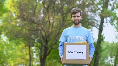Handsome Male Volunteer Holding Donation Box With Clothes Standing Outdoors