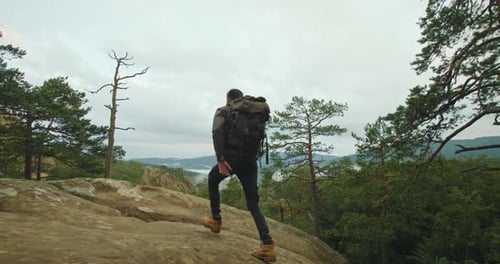 Un hombre va a la cima de un acantilado y mira el paisaje