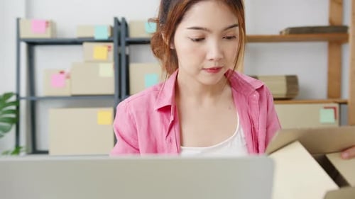 Woman Using Laptop While Holding Cardboard Box