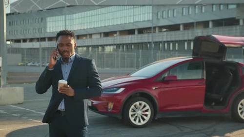 Glücklicher afrikanischer Unternehmer im stylischen Anzug trinkt heißen Kaffee und redet weiter