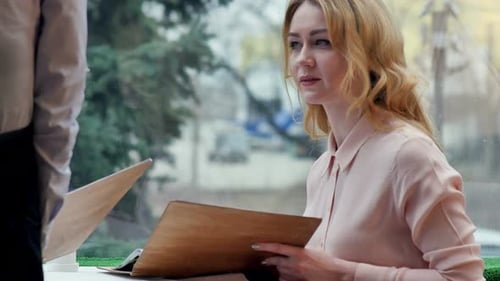 Cheerful Young Women Sitting at Cafe Holding Menu Card Giving Order To Waiter